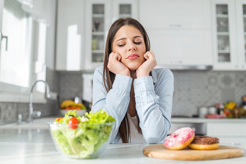 Woman looking at a salad and a donut, diet and weightloss myths