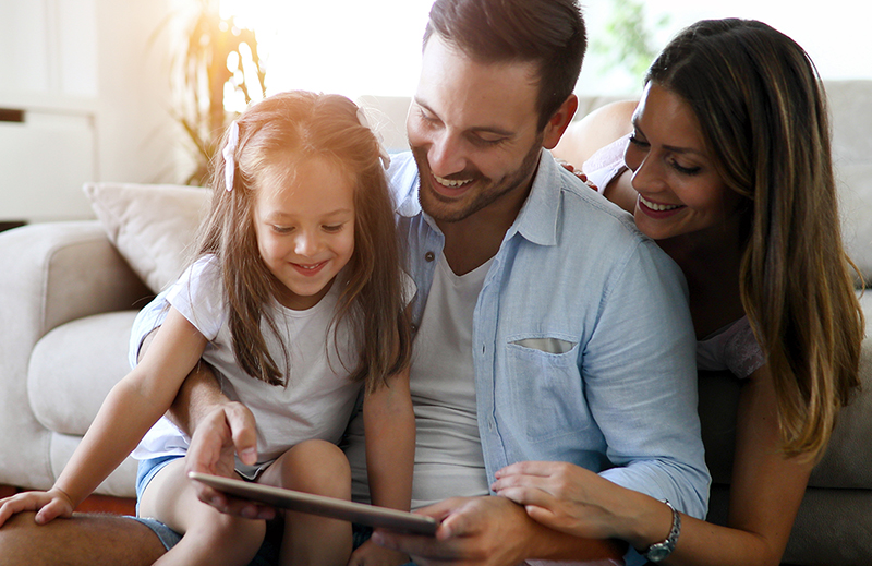 Family sitting on a couch looking at an tablet, learning their health insurance coverage options for if they've lost coverage