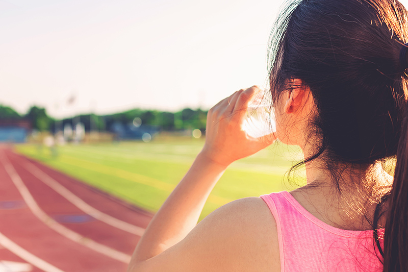 Woman drinking water and staying hydrated while running in the heat