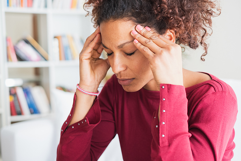 Woman suffers from migraine headaches and places fingers on head, 7 Things that May Help Prevent a Migraine
