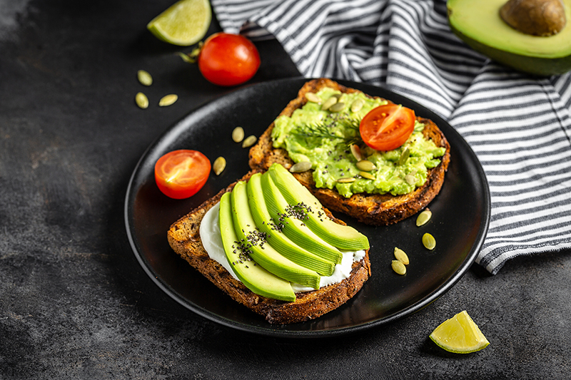 Avocado toast with tomatoes and goat cheese on a plate with a gray background