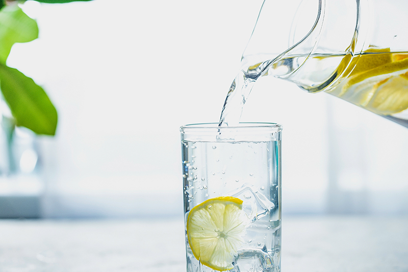 Pitcher of healthy lemon water being poured into a glass with ice.