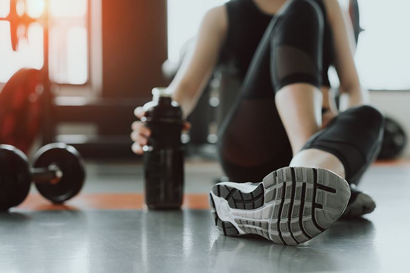Woman in workout clothes sitting on the floor next to weights and a water bottle
