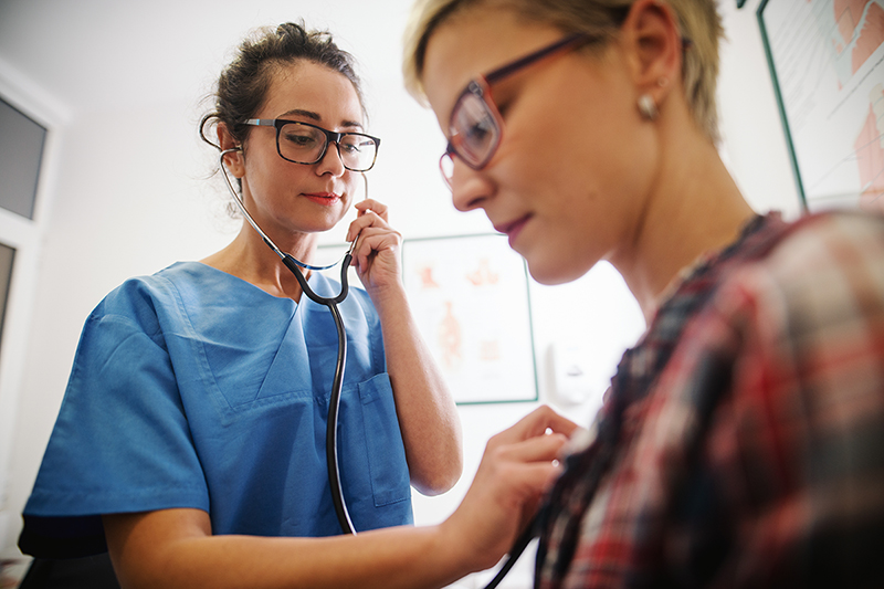 Female doctor uses stethoscope to listen to patient’s heart during a preventative checkup.