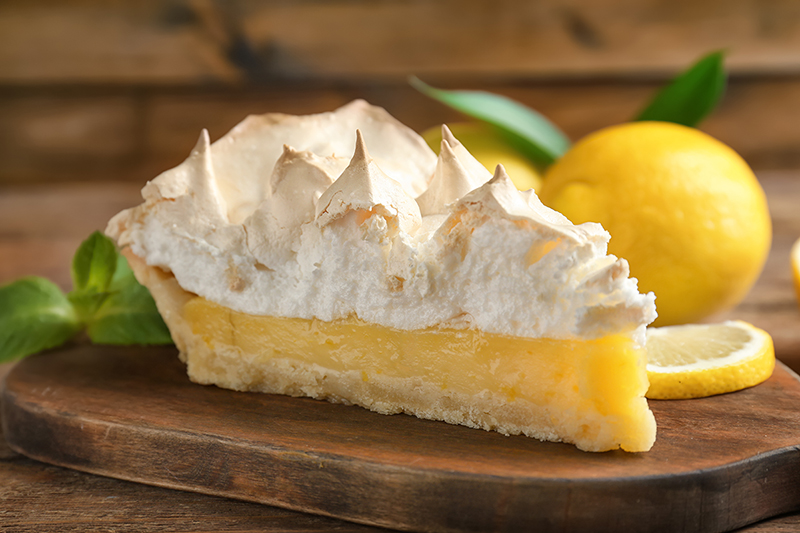 A fresh slice of lemon meringue pie on a wooden board.