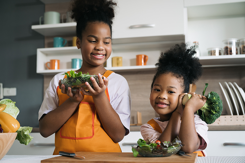 Happy sisters work in the kitchen to create healthy meals while having fun.