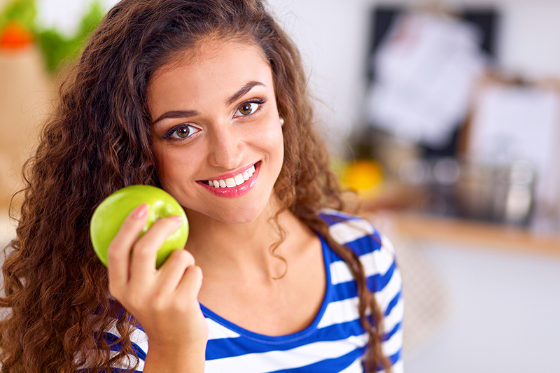 woman holding an apple in the kitchen, eating and apple a day helps her diet plan