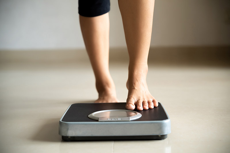 Female stepping on a weight scale to monitor belly fat.