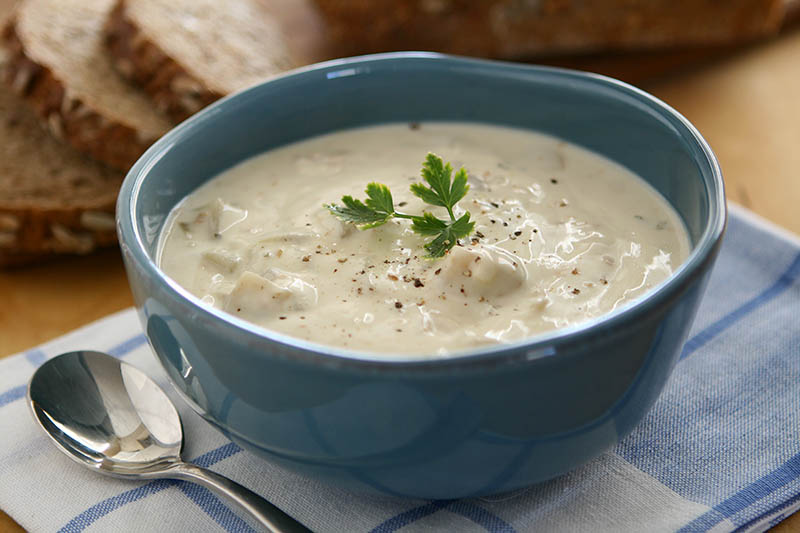 A warm bowl of seafood chowder sits on the table next to spoon.