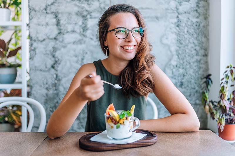 Woman sits at table eating breakfast.