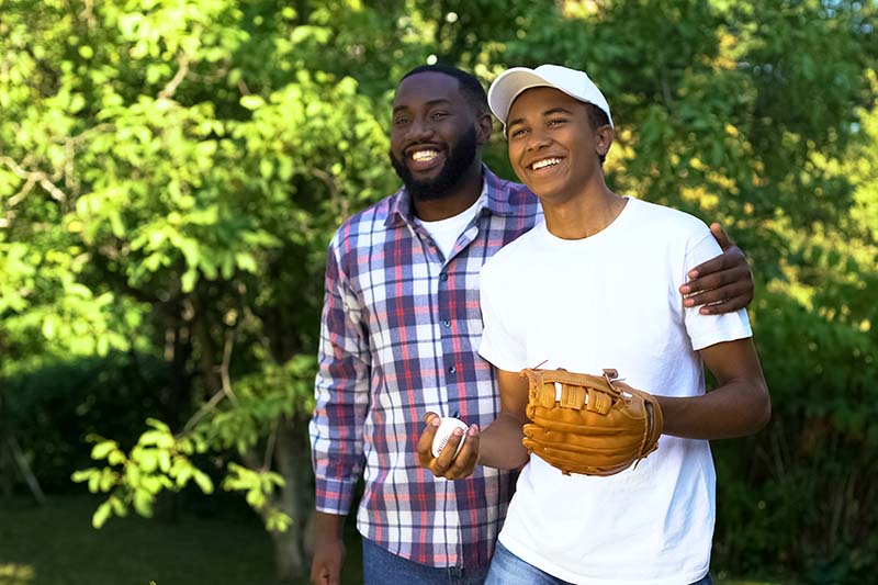 Smiling father supporting son with mental health challenges playing baseball.