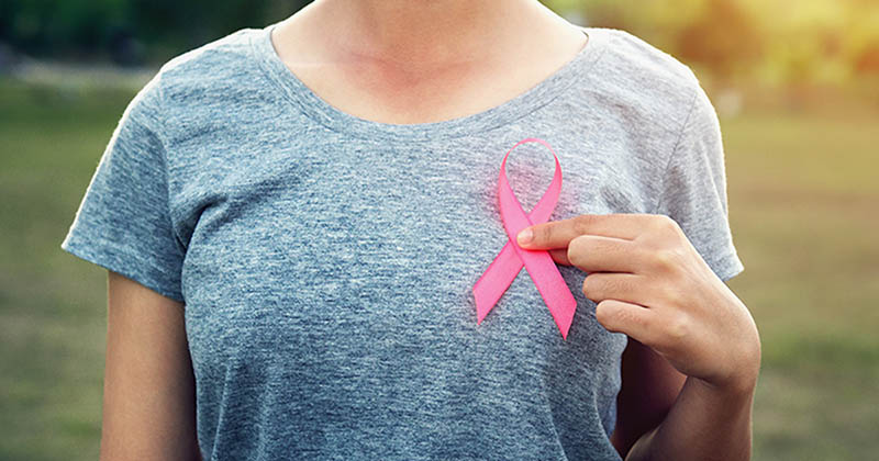 Woman holds pink breast cancer awareness ribbon up against chest.