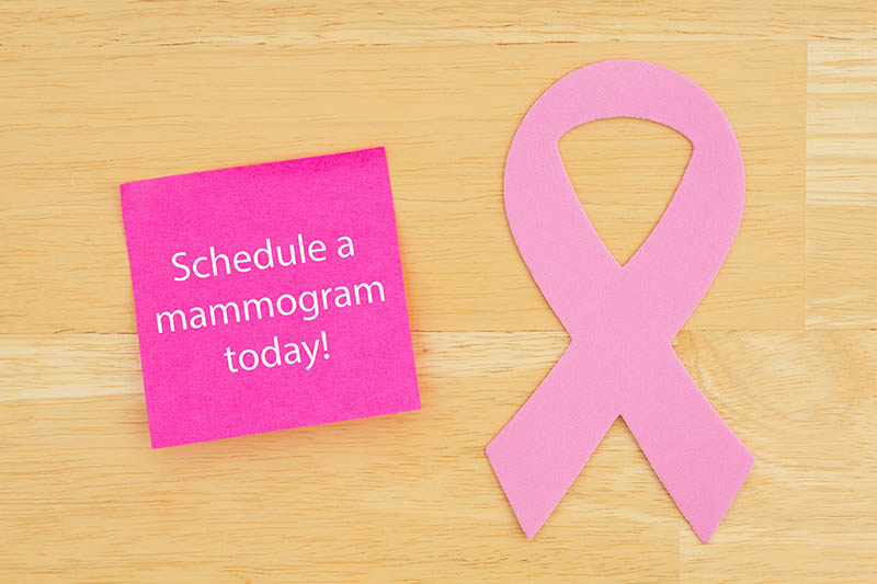 Pink mammogram reminder lays on table next to pink breast cancer awareness ribbon.
