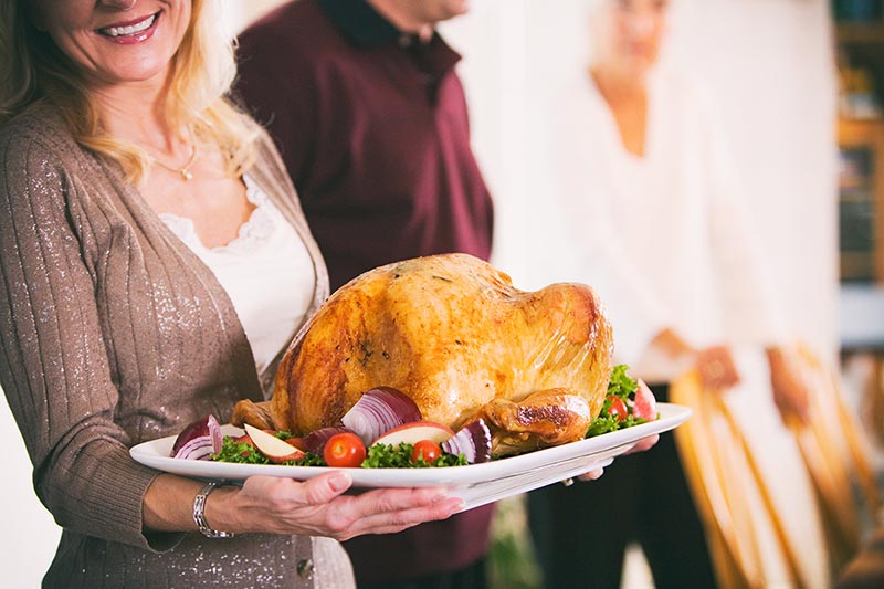 Woman holds platter with thanksgiving turkey.