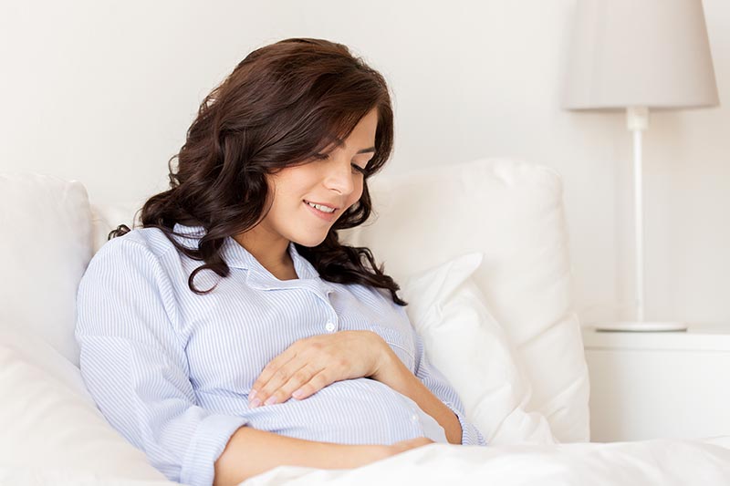 Mujer embarazada se sienta en la cama y mira la panza.