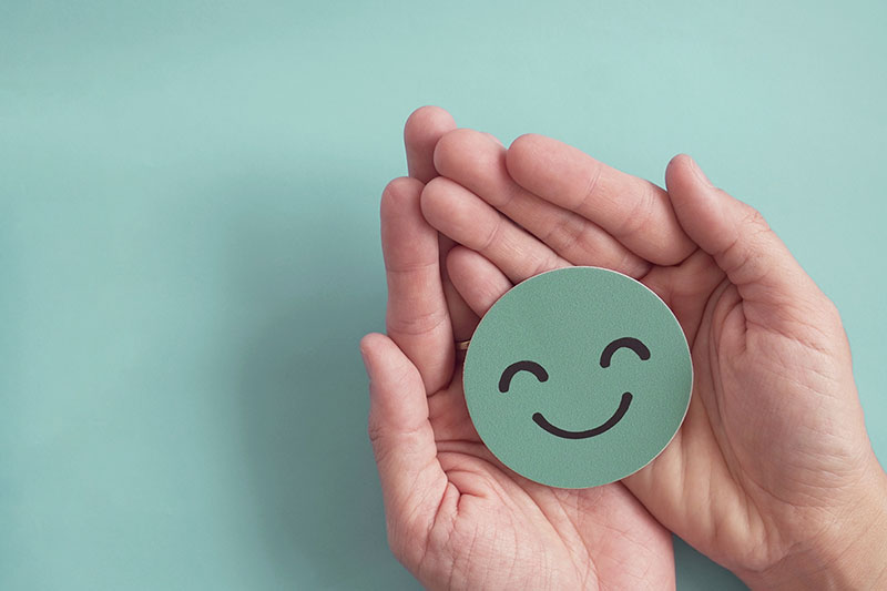 A positive smiley face is held in a lady’s hands.
