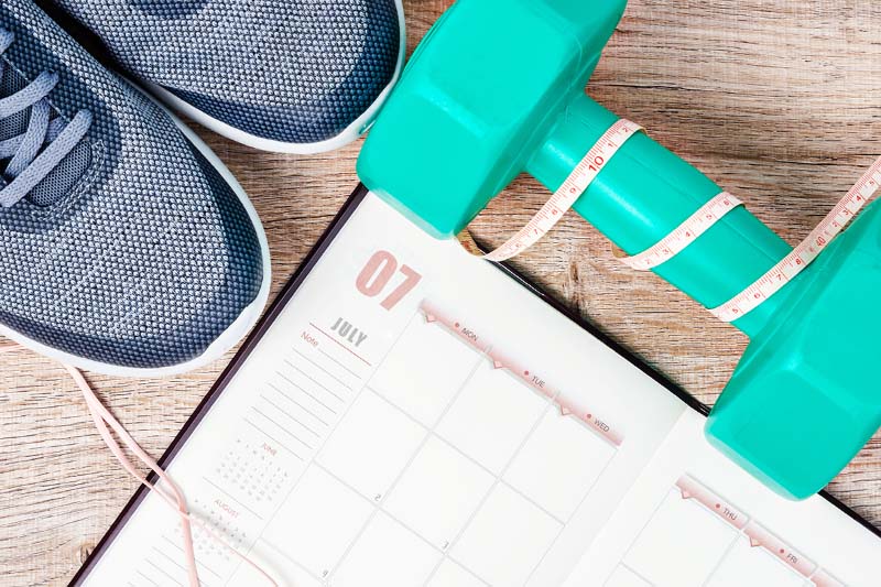 Green dumbbells and sneakers next to a blank exercise calendar.