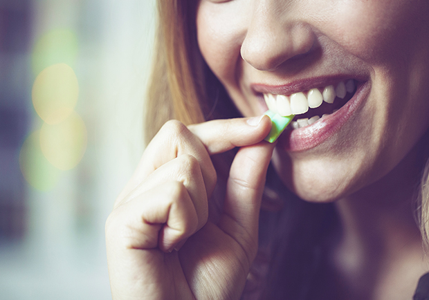 Woman putting a piece of gum into her mouth. What are the surprising benefits of chewing gum? 