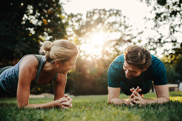 Happy couple planking in the park, one of the suggested ways to lose belly fat