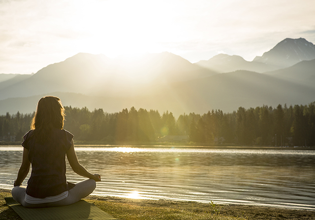 Girl sitting next to lake meditating, the benefits of meditation