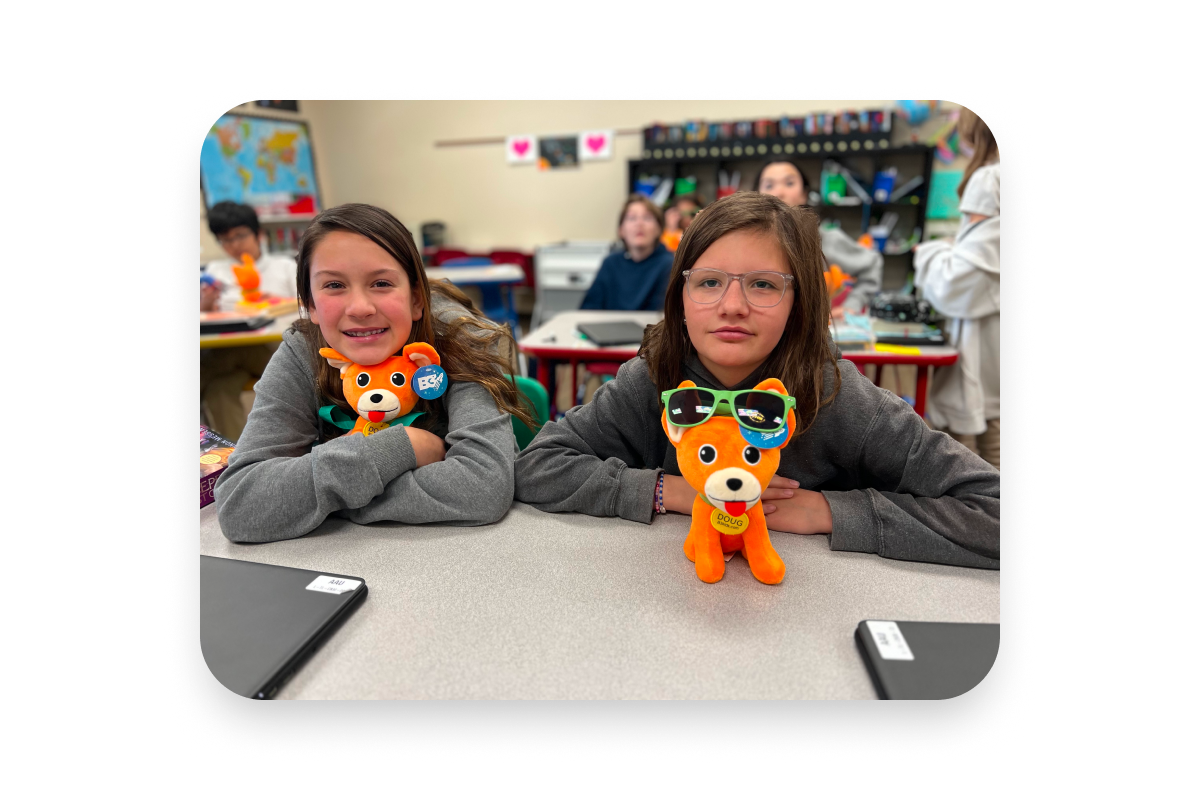  two girls sitting at table in classroom holding stuffed dogs