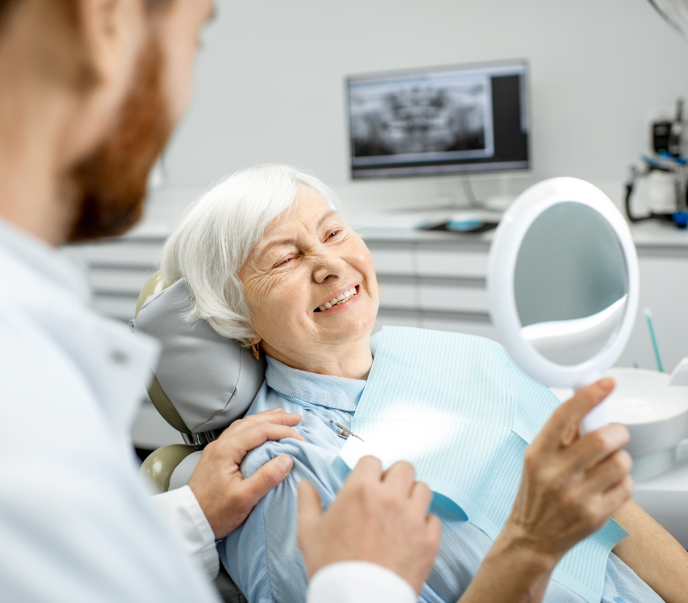Woman at a dentist office smiling and looking in a mirror