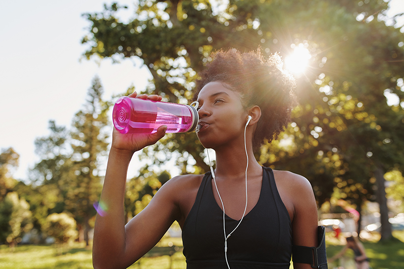 Woman exercising in the summer heat, drinking from a water bottle